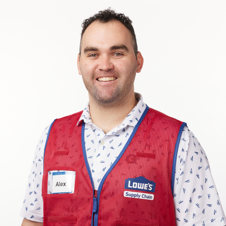 A person wearing a red vest over a white and blue patterned shirt stands against a white background.