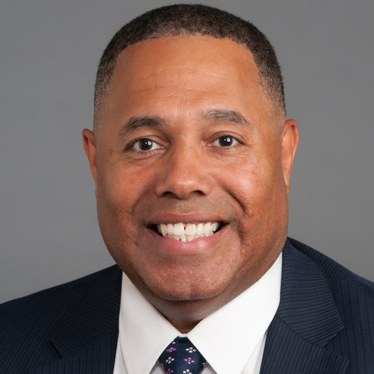 A headshot of a man in a suit and tie, smiling broadly.