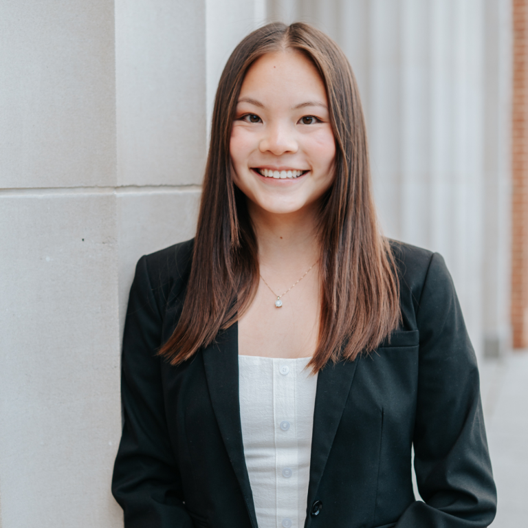A young person wearing a black blazer over a white shirt smiles at the camera.